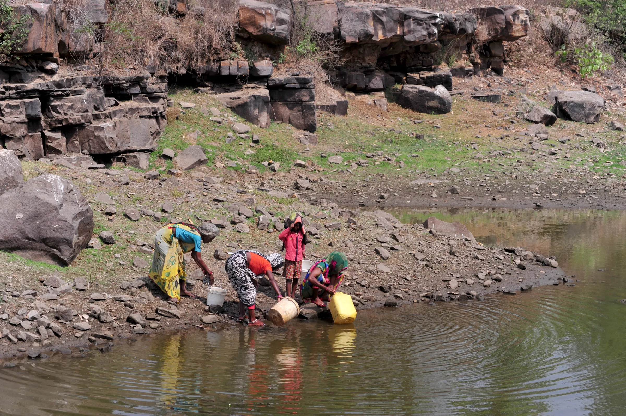 Women and a girl fill containers with water from an abandoned stone quarry on a hot day in Badama village